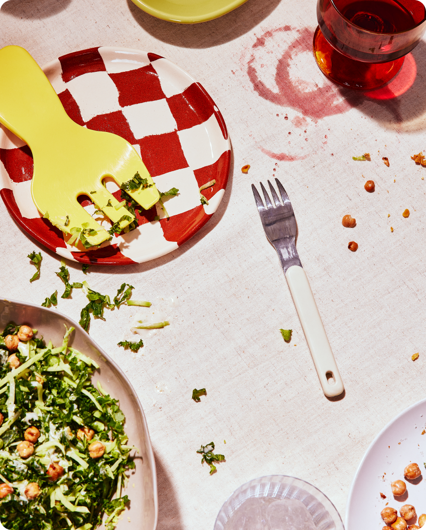 Checkered plate with yellow fork, salad, and a white-handled fork on a light surface.
